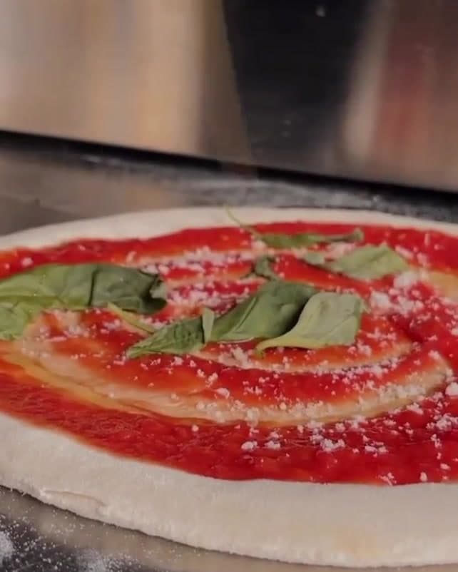 A margherita being topped with basil and olive oil before going into the wood-fired oven