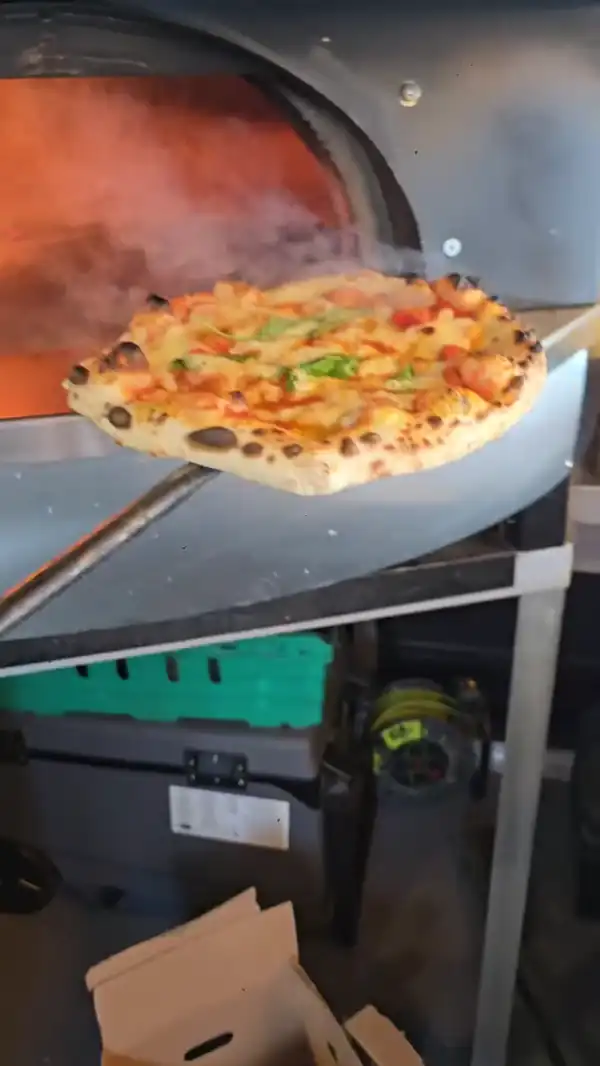 A Neapolitan pizza coming out of the wood-fired oven on the peel